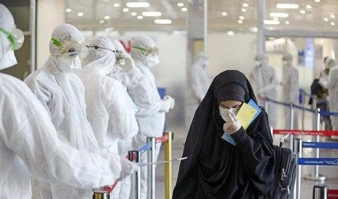 Medical staff in protective gears distribute information sheets to Iraqi passengers returning from Iran at Najaf International Airport on Friday. (AFP)