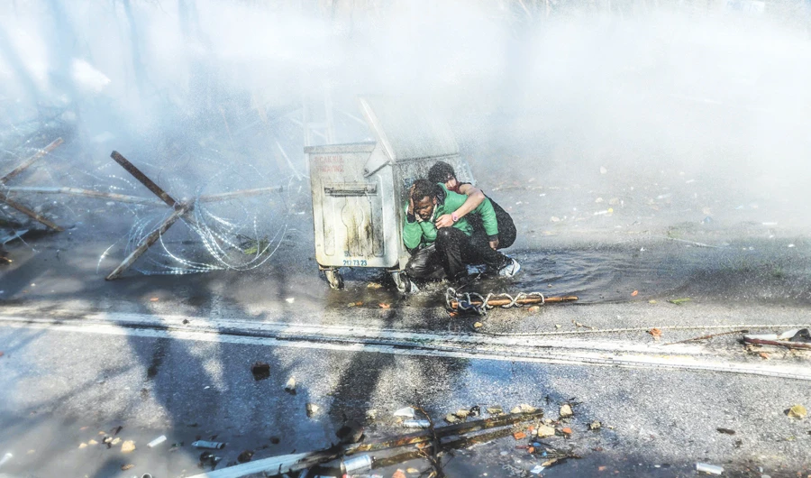 Migrants take cover behind a container as Greek police uses water cannon to block them trying to break fences in the border province of Edirne. (AFP)
