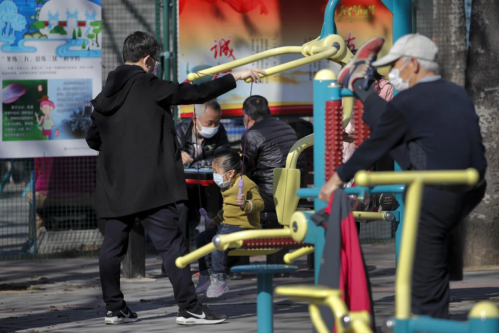 Residents wearing protective face masks play on an exercise equipment set up for public use at a park in Beijing on March 15, 2020. (AP Photo/Andy Wong)