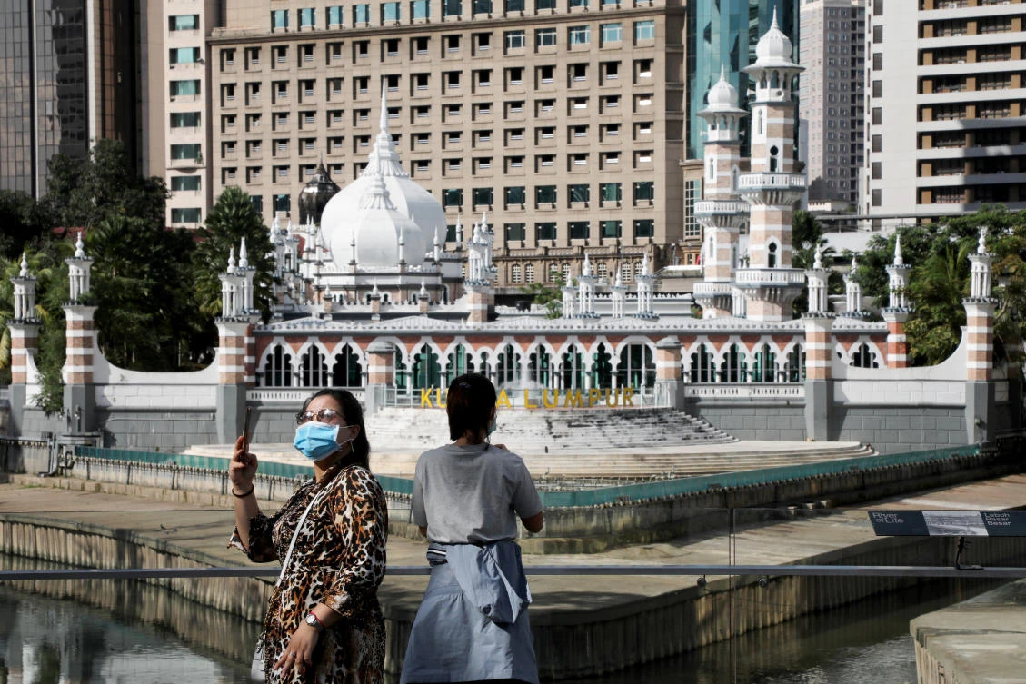 Tourists wearing protective masks take pictures outside a mosque following the outbreak of coronavirus, in Kuala Lumpur, Malaysia March 16, 2020. (Reuters)