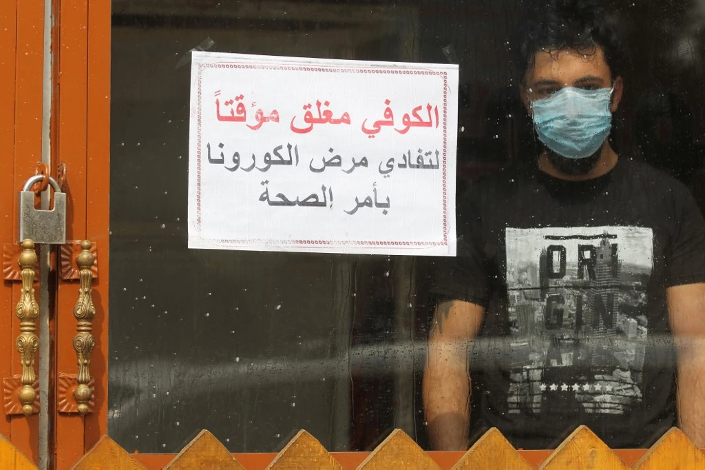 A Baghdad resident stands inside a coffee shop with a sign in Arabic which reads ‘Coffee shop is closed, due to corona following a decision by the health ministry’ on March 16, 2020. (AFP)