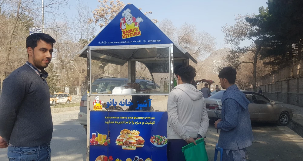 Two men wait for their food order from Banu’s Kitchen rickshaw on a street in Kabul on Saturday. (AN photo)