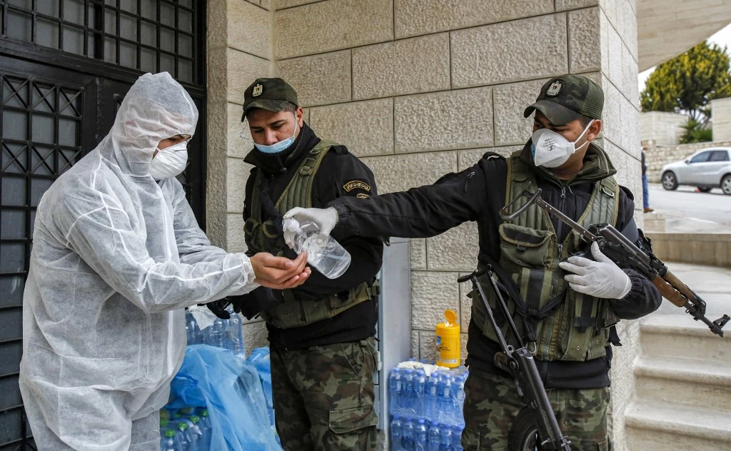 A member of the Palestinian security forces applies antiseptic gel to his hands while being assisted to wear a protective suit before delivering food supplies to a hotel under quarantine due to COVID-19 in Beit Jala, Bethlehem. (File/AFP)