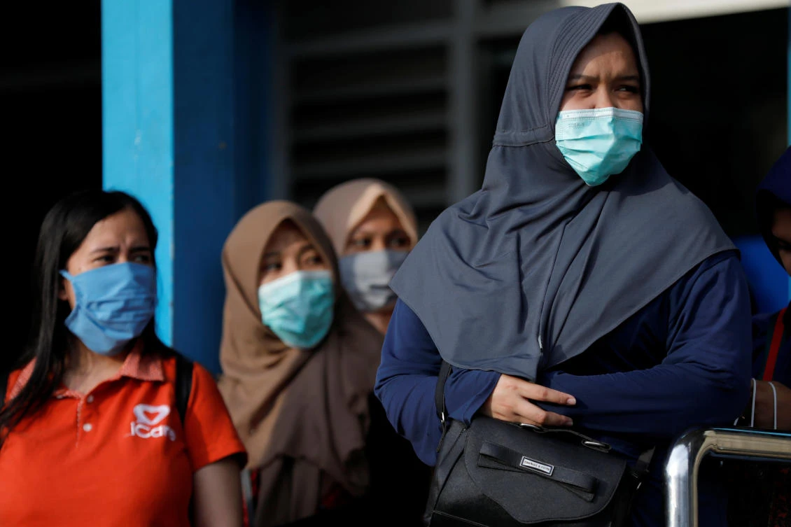 Women wearing face masks stand as they queue for public bus amid the spread of coronavirus disease (COVID-19) in Jakarta, Indonesia March 18, 2020. REUTERS/Willy Kurniawan