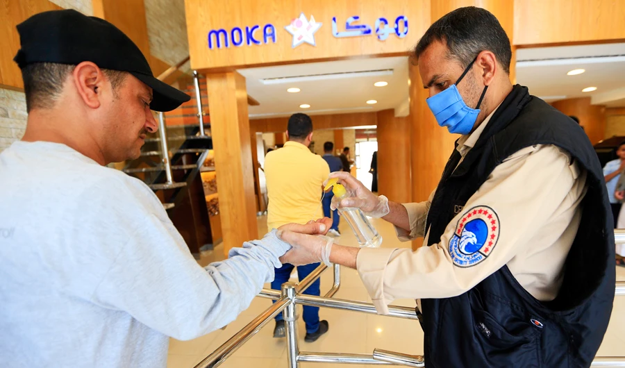 A security guard wearing a protective mask sprays sanitizer onto the hands of incoming customers as a measure against COVID-19 coronavirus disease, outside a coffee shop in Yemen's capital Sanaa on March 19, 2020. (AFP)