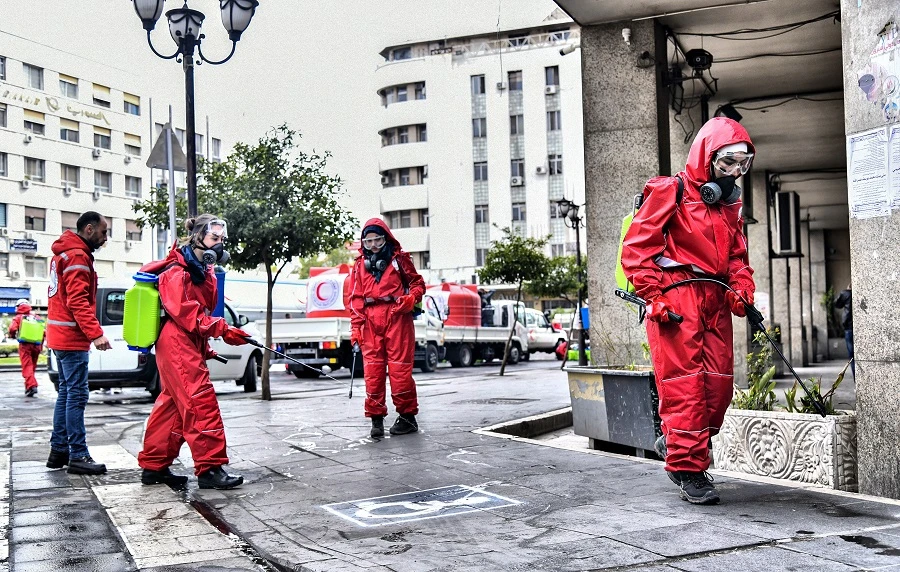 A handout picture released by the official Syrian Arab News Agency (SANA) on March 20, 2020 shows Syrian Red Crescent workers spraying disinfectant along a street in the capital Damascus, as part of measures against the spread of COVID-19. (File/AFP)