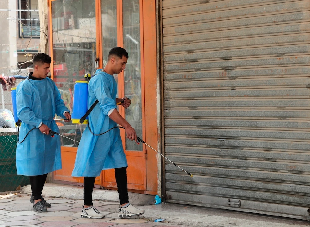 Iraqi volunteers spray disinfectant as a precaution against the coronavirus during a curfew, in a market in Baghdad, Iraq, Sunday, March 22, 2020. (AP)
