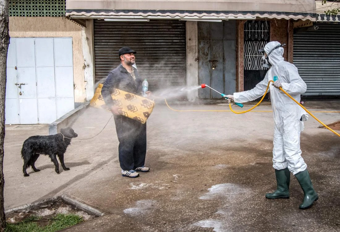 A Moroccan health ministry worker disinfects a man walking a dog and carrying a mat in the capital Rabat on March 22, 2020. (AFP)