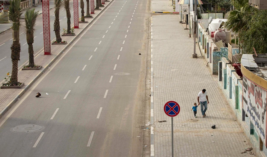 A father walks with his child along a deserted street in Iraq’s southern city of Basra during a curfew imposed as a measure to stem the spread of the coronavirus. (AFP)