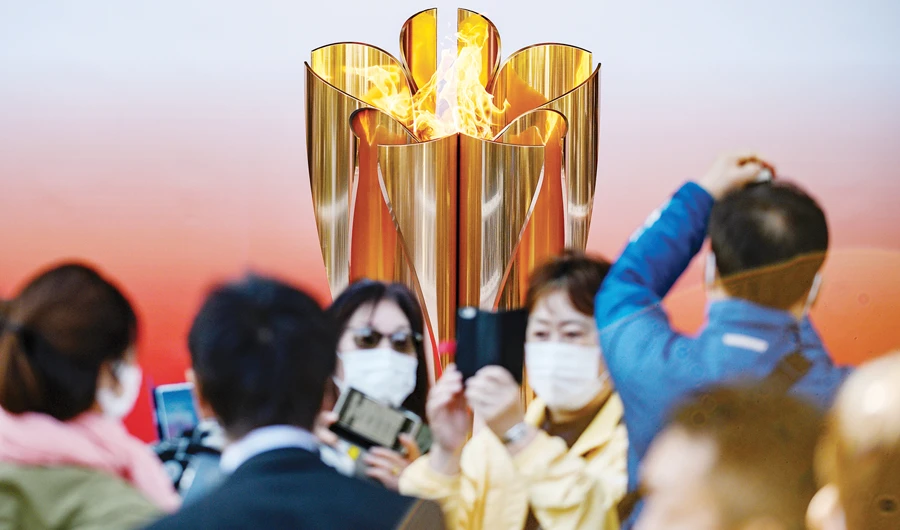 People wearing face masks take pictures in front of the Tokyo 2020 Olympic flame, which is displayed outside Sendai railway station. (AFP)