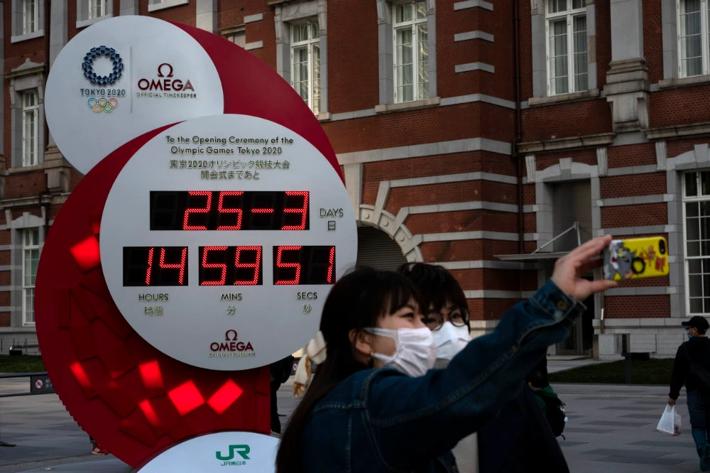 Two women take a selfie with a Tokyo 2020 countdown clock displaying the current date instead of the countdown days. (AP)