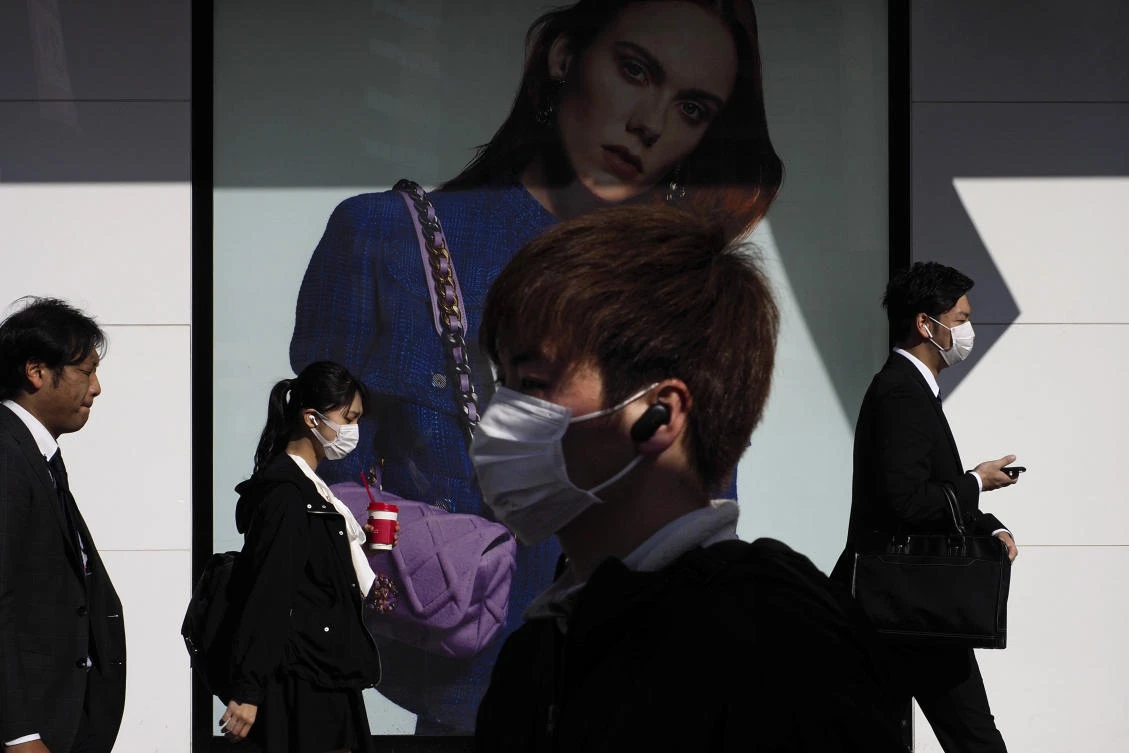 Commuters walk past an advertisement outside Shinjuku Station Thursday, March 26, 2020, in Tokyo. (AP)