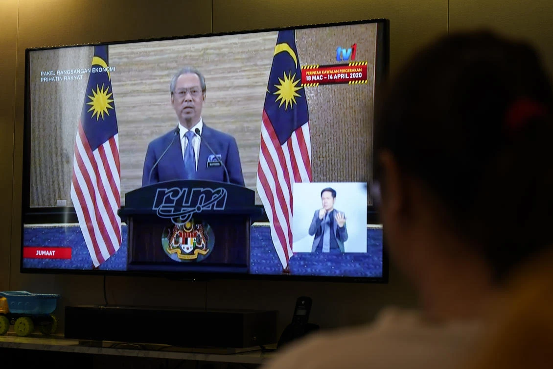 People watch live telecast of Malaysian Prime Minister Muhyiddin Yassin’s speech on COVID-19 stimulus package in Kuala Lumpur on Friday, March 27, 2020. (AP)