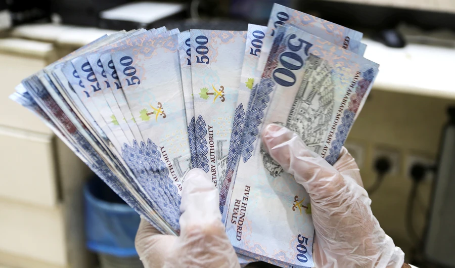 A Saudi money exchanger wears gloves as he counts Saudi riyal currency at a currency exchange shop in Riyadh, Saudi Arabia March 10, 2020. (REUTERS)