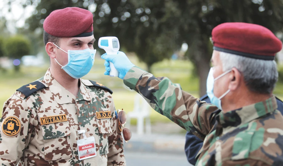 An Iraqi soldier checks the temperature of an officer in Baghdad during a curfew imposed to prevent the spread of the coronavirus disease. (Reuters)