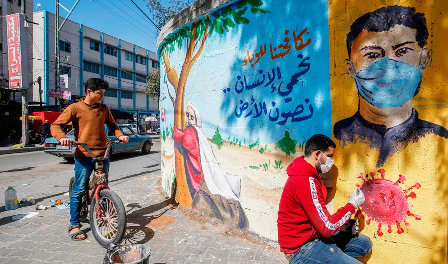 A Palestinian artist paints a mural in the southern Gaza Strip, reading ‘by fighting the epidemic, we protect the human being and preserve the earth.’ (AFP)