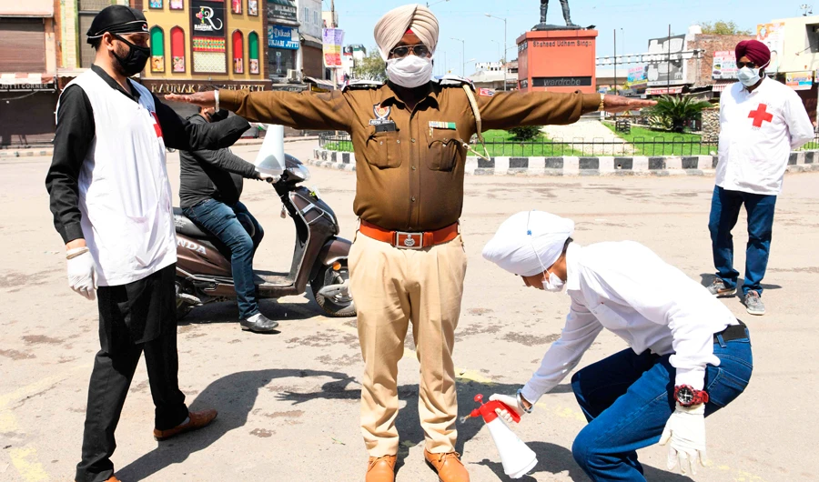 A volunteer sprays disinfectant on a policeman at a street during a government-imposed nationwide lockdown in Amritsar on Saturday. (AFP)