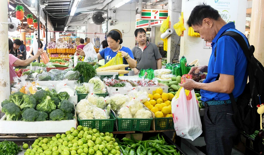 This photograph taken on February 18, 2020 shows people buying vegetables at a market in Singapore. Singapore’s central bank eased monetary policy on March