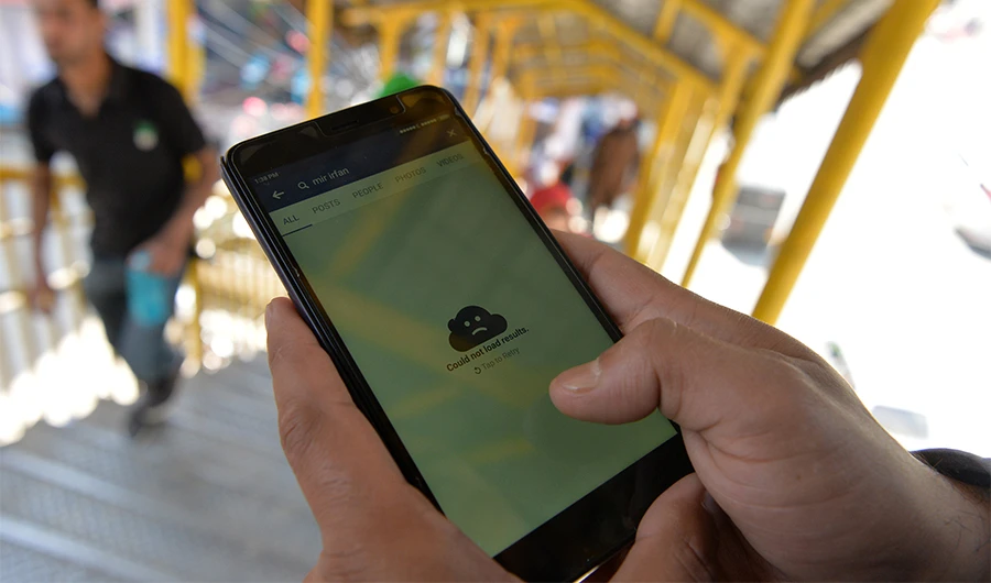 An Kashmiri man browses blocked services on the internet on his mobile phone on a footbridge in Srinagar on April 27, 2017. (AFP)