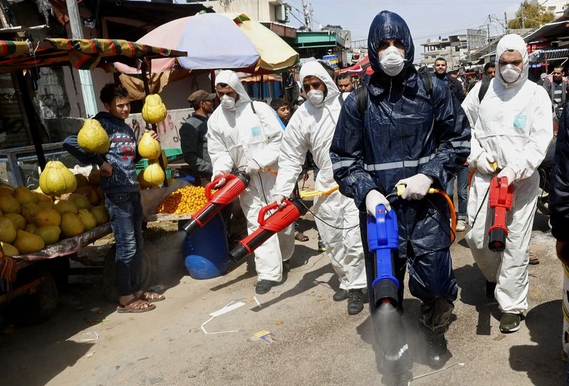 In this Thursday, March 19, 2020 file photo, workers wearing protective gear spray disinfectant as a precaution against the coronavirus, at the main market in Gaza City. (AP)