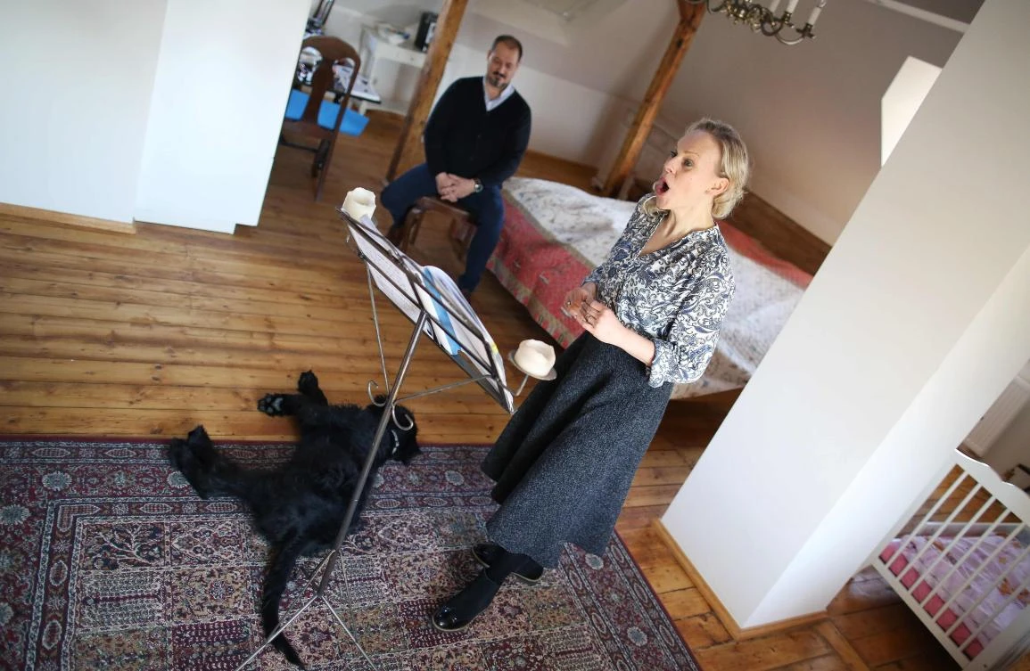 German sopranist and member of the ensemble of Leipzig's opera house (Oper Leipzig), Lilli Wuenscher sings next to her husband Canadian bass Randall Jakobsh at home, where the family stays confined due to the pandemic of the novel coronavirus, on April 3, 2020 on the outskirts of Leipzig, eastern Germany. The gates of the Leipzig Opera have been closed for about three weeks due to the novel corona pandemic - but the voices and instruments of the artists are far from silent. / AFP / Ronny Hartmann