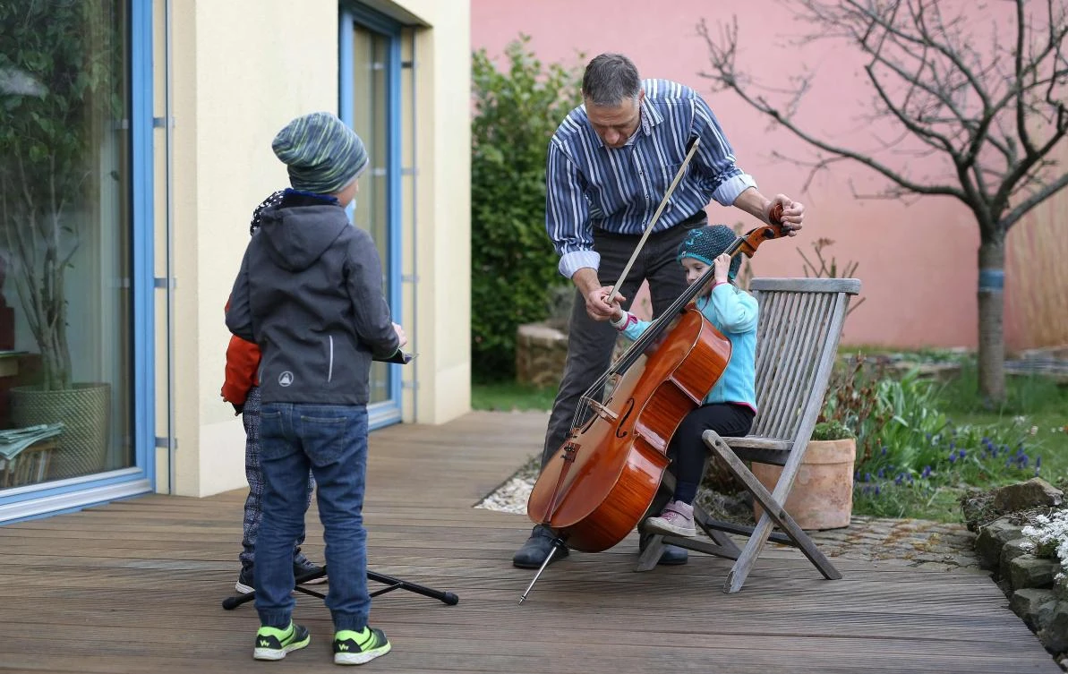 German musician Stephan Wuensch, principal cellist of Leipzig's opera house (Oper Leipzig), plays the violoncello as children from the neighbourhood listen, on April 3, 2020 at his home on the outskirts of Leipzig, where he stays confined due to the pandemic of the novel coronavirus. The gates of the Leipzig Opera have been closed for about three weeks due to the novel corona pandemic - but the voices and instruments of the artists are far from silent. / AFP / Ronny Hartmann