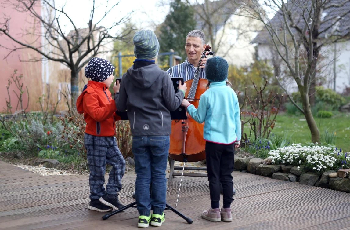 German musician Stephan Wuensch, principal cellist of Leipzig's opera house (Oper Leipzig), plays the violoncello as children from the neighbourhood listen, on April 3, 2020 at his home on the outskirts of Leipzig, where he stays confined due to the pandemic of the novel coronavirus. The gates of the Leipzig Opera have been closed for about three weeks due to the novel corona pandemic - but the voices and instruments of the artists are far from silent. / AFP / Ronny Hartmann