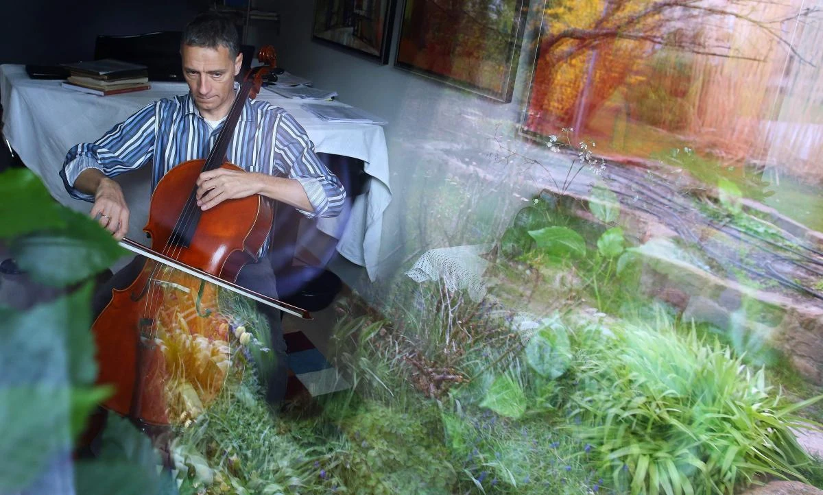German musician Stephan Wuensch, principal cellist of Leipzig's opera house (Oper Leipzig), is seen through a window as he plays the violoncello at home, where he stays confined with his family due to the pandemic of the novel coronavirus, on April 3, 2020 on the outskirts of Leipzig, eastern Germany. The gates of the Leipzig Opera have been closed for about three weeks due to the novel corona pandemic - but the voices and instruments of the artists are far from silent. / AFP / Ronny Hartmann