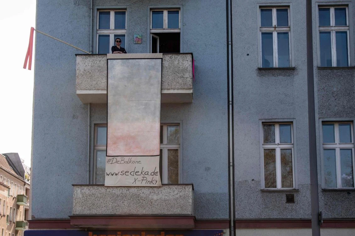 Berlin-based Polish artist Isabella Sedeka stands on her balcony as she displays her work, part of the "Balconies, Life, Art, Pandemic, and Proximity" exhibition, in Berlin on April 12, 2020, amid a new coronavirus COVID-19 pandemic. Over 30 artists are taking part in the two-day exhibition which calls on "the artistic community living in [Berlin's district of] Prenzlauer Berg to activate / exhibit / inhabit / their windows and balconies on Easter Sunday and Monday". Curated by Ovul Durmusoglu and Joanna Warsza, the exhibition boasts "zero budget, no openings, no crowds, just a proposition of a stroll that would connect dots in solidarity and togetherness". / AFP / John MACDOUGALL