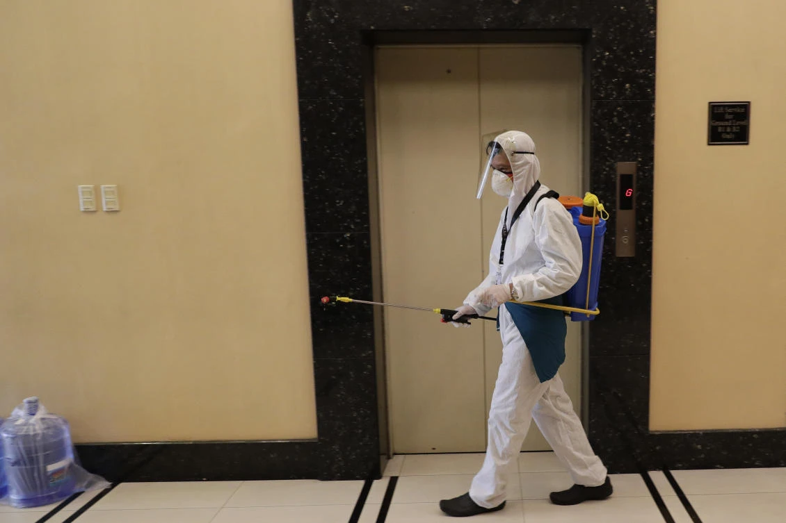 A man wearing protective suit sprays disinfectants at the entrance of a building to help curb the spread of the new coronavirus in Manila, Philippines on Wednesday, April 1, 2020. (AP)