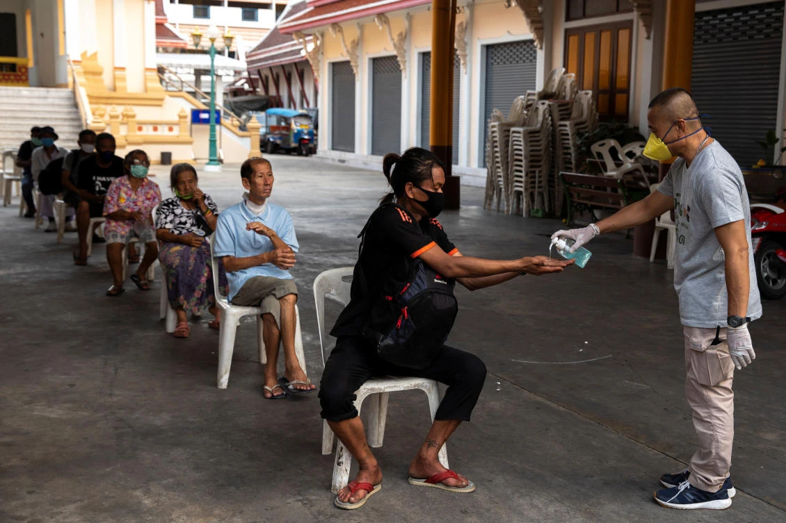 A volunteer wearing a face mask gives hand gels to homeless people before they receiving food at the Wat Arun Ratchavararam in Bangkok, Thailand on April 2, 2020. (Reuters)