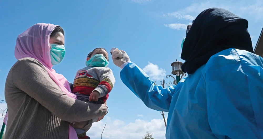 A doctor checks the body temperature of an 8-month-old boy in the arms of his mother after they completed 14 days of quarantine on the outskirts of Srinagar. (AFP)