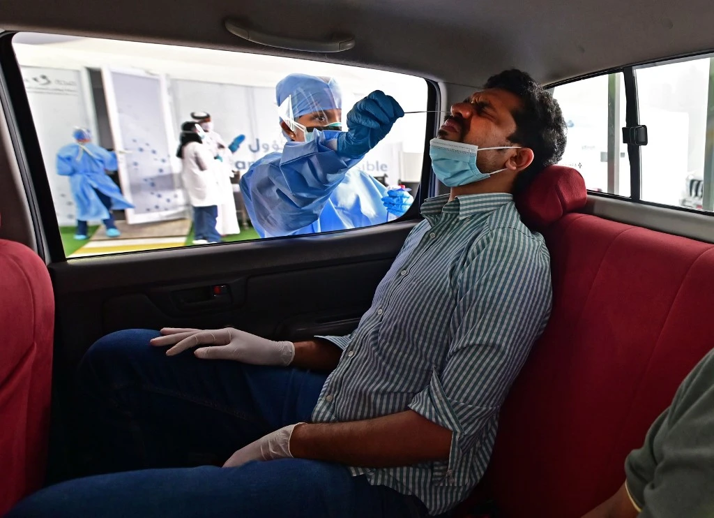 Above, a nurse uses a swab to test the passenger of a car for coronavirus at a drive-thru verification center in Abu Dhabi on April 2, 2020. (AFP)