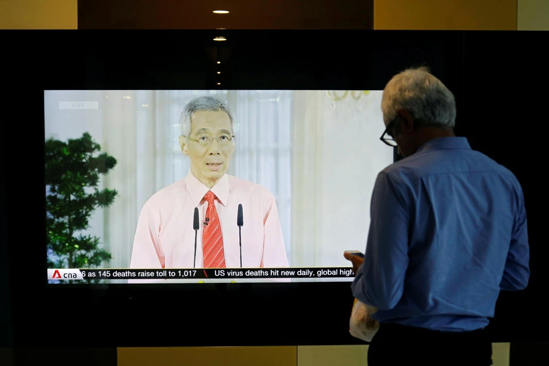 A man stands in front of a screen showing a telecast of Singapore’s Prime Minister Lee Hsien Loong addressing the outbreak of coronavirus in Singapore on April 3, 2020. (Reuters)