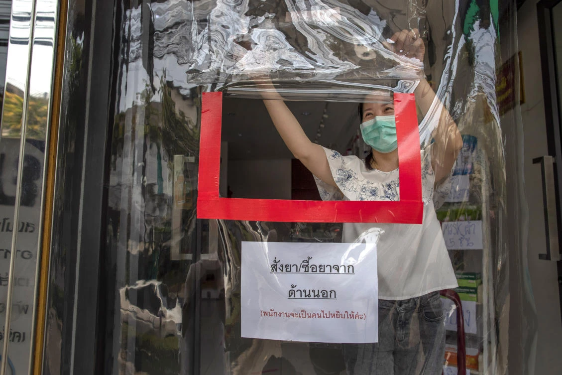 A pharmacist opens a service window through a plastic sheet covering the entrance to help practice social distancing in Bangkok, Thailand on April 2, 2020. (AP)