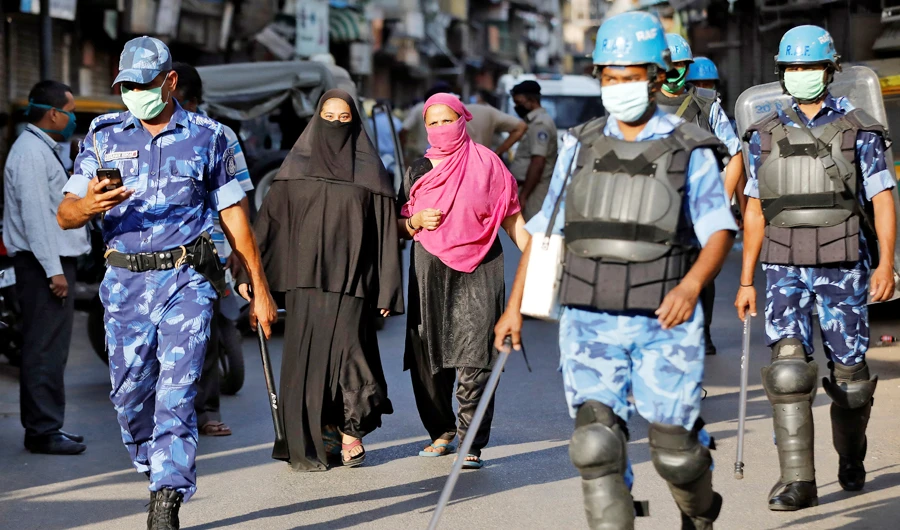 Veiled Muslim women walk near members of Rapid Action Force patrolling a neighborhood during a lockdown in the area in Ahmedabad on Monday. (Reuters)