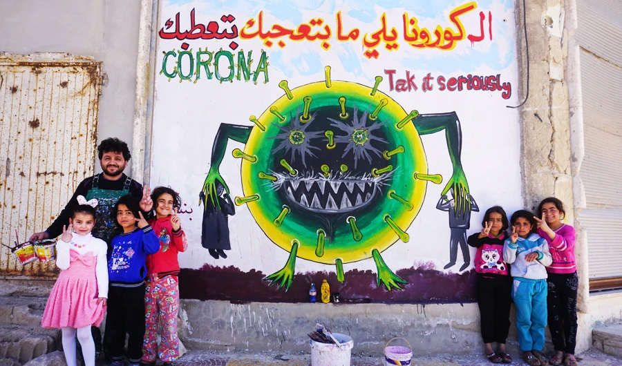 Syrian artist Aziz Al-Asmar and children flash the victory gesture next to freshly drawn graffiti of a cartoon depiction of coronavirus, in Idlib province on March 23. (AFP)