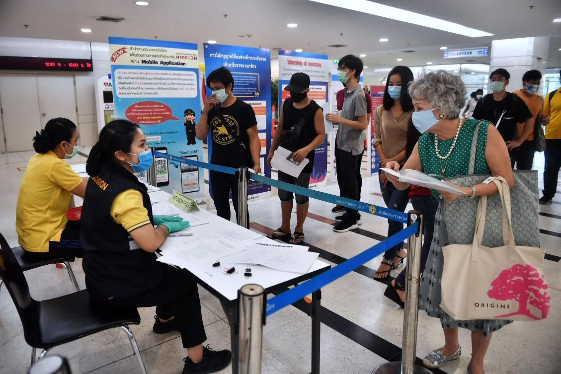 Above, people wearing face mask stand in line to renew their visas at the Government Immigration Center in Bangkok on April 8, 2020. (AFP)