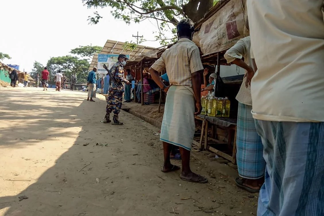 A security personnel (C) patrols in an alley as Rohingya refugees buy groceries from shops during a government-imposed lockdown of Cox's Bazar district as a preventive measure against the COVID-19 coronavirus, in Ukhia on April 9, 2020. (AFP)