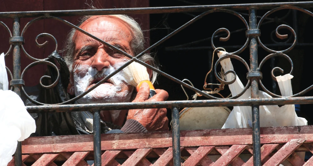 An elderly man applies shaving foam as he sits on his balcony in Sidon on Thursday during a countrywide lockdown to combat the spread of the coronavirus disease. (Reuters)