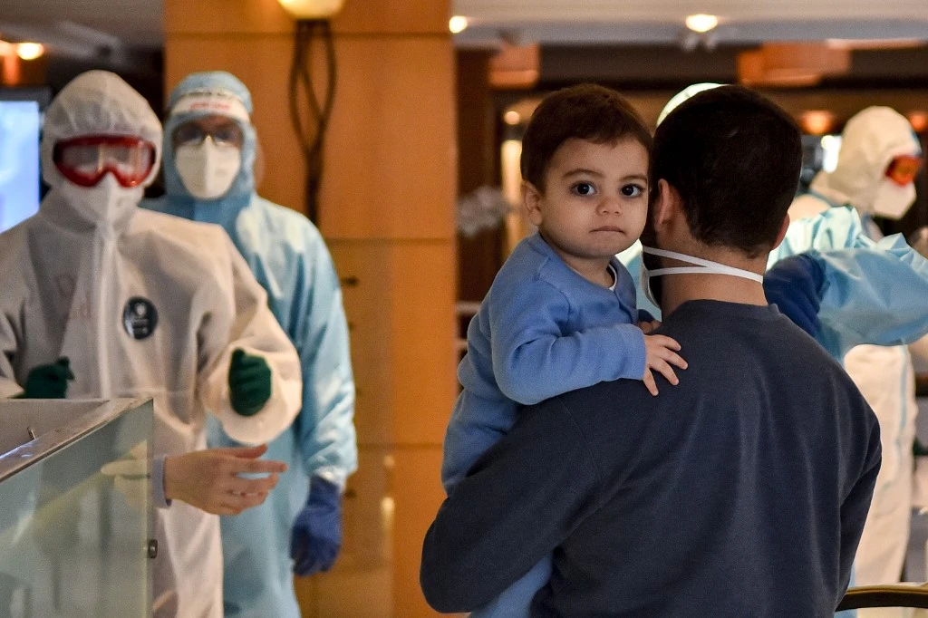A man carries a child as he arrives, along with other Lebanese nationals repatriated from Qatar, at a hotel in the Lebanese capital Beirut on April 9, 2020, to be quarantined. (AFP)