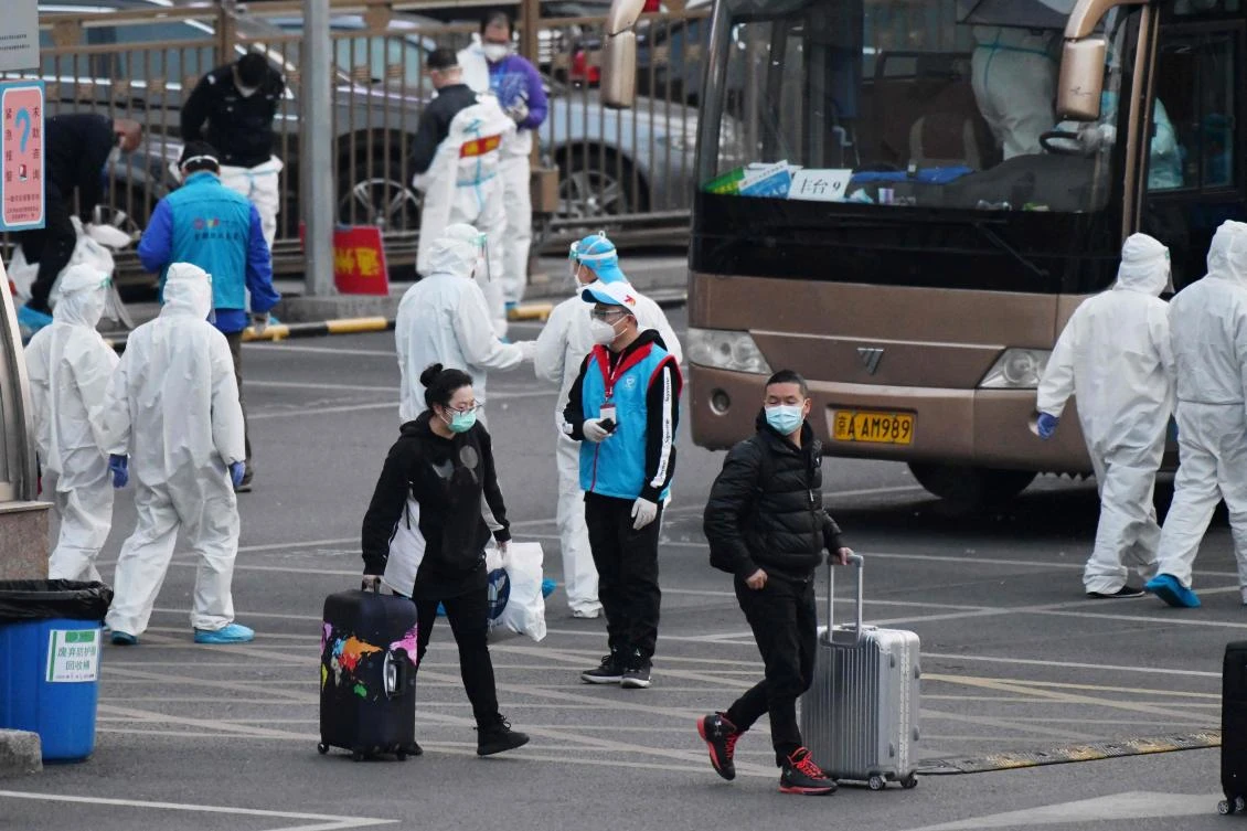 Travelers arriving from Hubei province walk past workers in hazmat suits to buses taking them to their individual districts, at Beijing West Railway Station on April 10, 2020. (AFP)