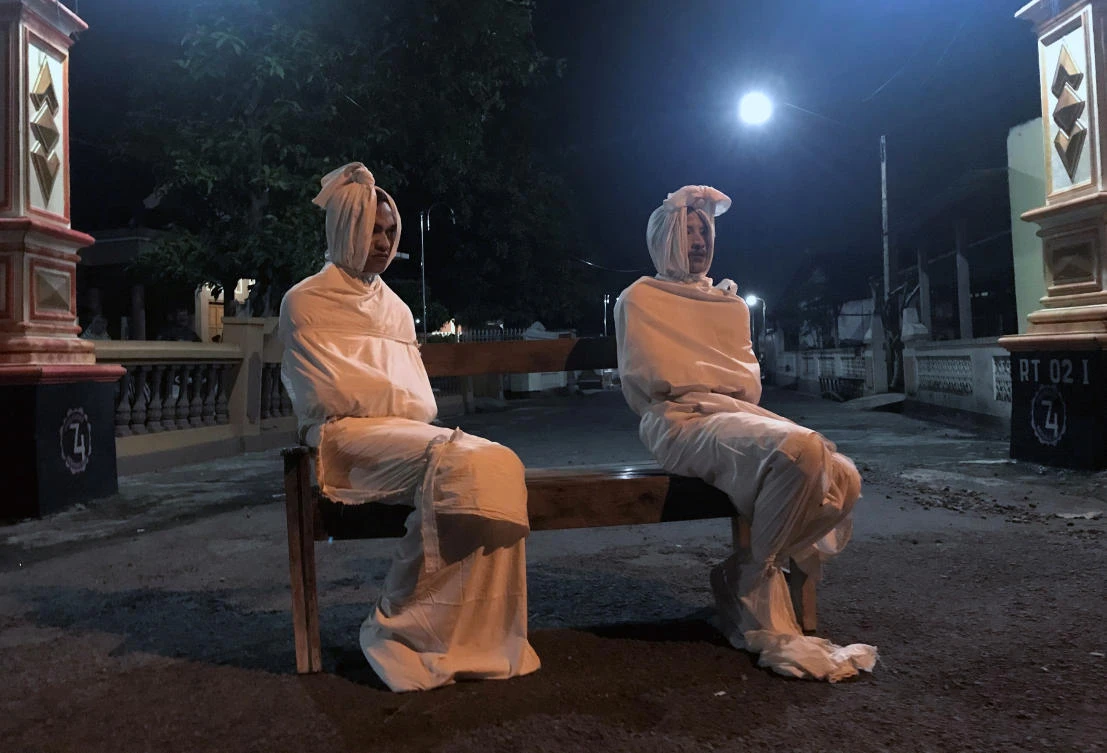Volunteers Deri Setyawan, 25, and Septian Febriyanto, 26, sit on a bench as they play the role of ‘pocong’, or known as ‘shroud ghost’, to make people stay at home. (Reuters)