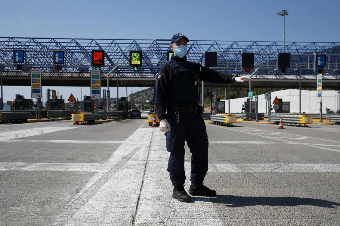 A policeman wearing a face mask to protect from coronavirus stops a car at a roadblock in Elesfina toll stations, west of Athens, Friday, April 10. 2020. (AP)