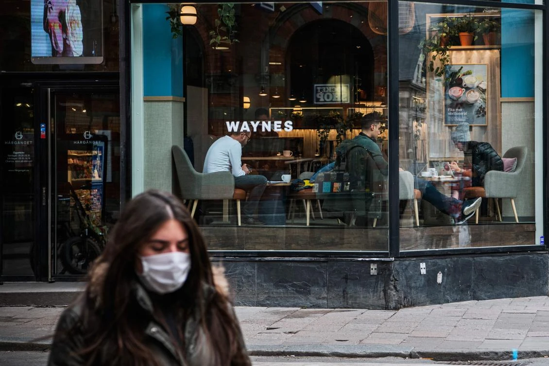 A woman wearing a protective mask walks in Sodermalm near a busy coffee shop on April 14, 2020, in Stockholm amid the novel coronavirus COVID-19 pandemic. / AFP / Jonathan NACKSTRAND