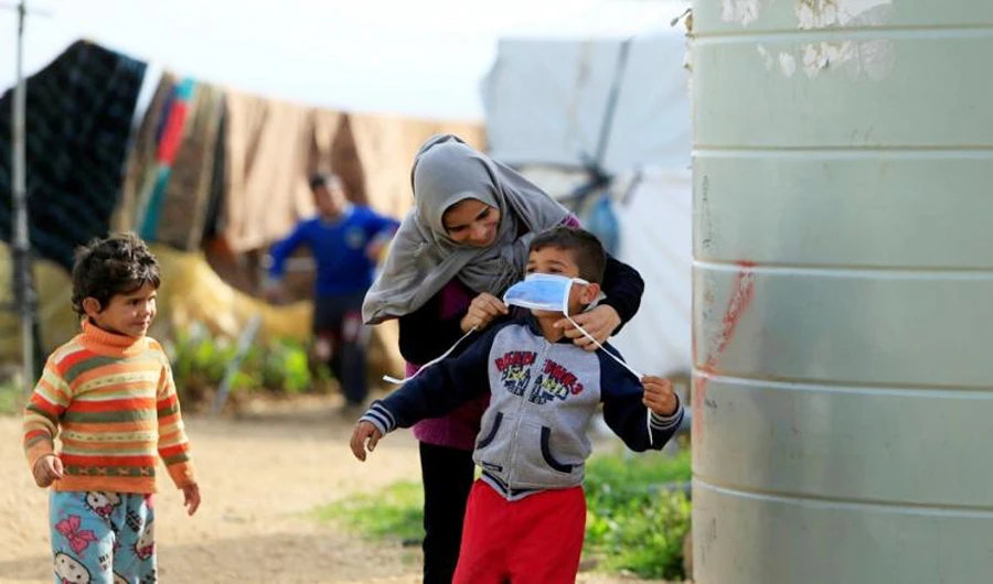 A Syrian refugee helps a child put on a face mask in Al-Wazzani, Lebanon. (Reuters)