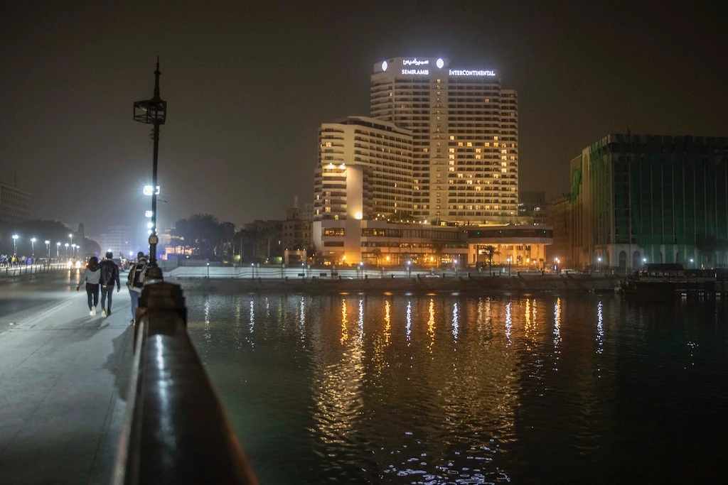In this March 23, 2020 photo, a couple walk on Kasr El Nile Bridge near a lit hotel displaying a heart for the coronavirus outbreak, in Cairo, Egypt. (AP)