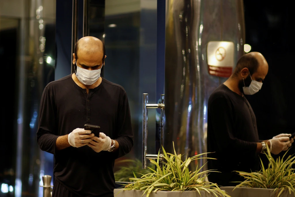 A man wearing a protective mask and gloves checks the app "Be Aware" on his smartphone, launched by Bahrain's health authorities to contain the coronavirus disease (COVID-19) by spreading awareness and sharing updates on the situation, at a hotel in Manama, Bahrain, April 19, 2020. (Reuters)