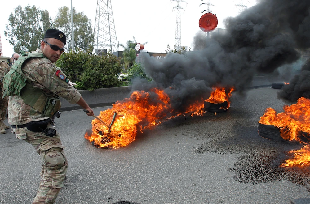 A Lebanese soldier tries to open a highway blocked by burning tires in Zouk, north of Beirut Monday. (Reuters)