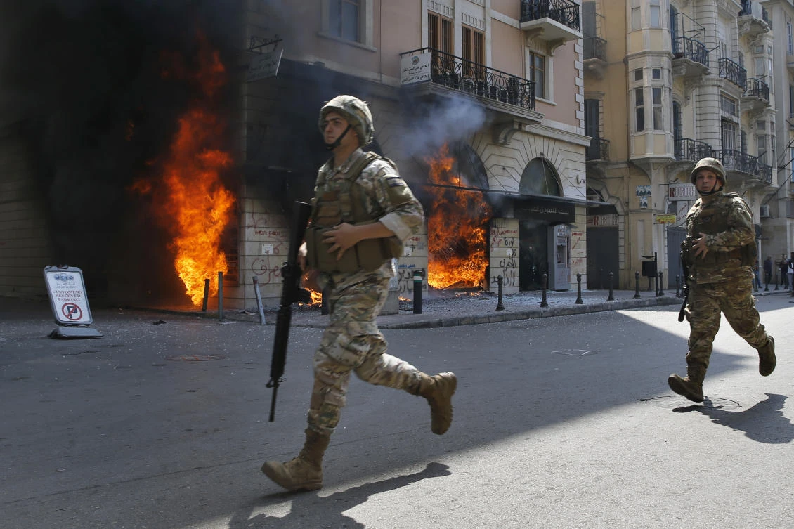 Lebanese army soldiers run in front of a Credit Libanais Bank that was set on fire by anti-government protesters, in the northern city of Tripoli, Lebanon, Tuesday, April 28, 2020. Hundreds of angry Lebanese took part Tuesday in the funeral of a young man killed in riots overnight in the northern city of Tripoli that were triggered by the crash of Lebanon's national currency that sent food prices soaring. (AP)